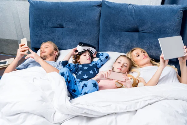 Familia con aparatos en la cama - foto de stock