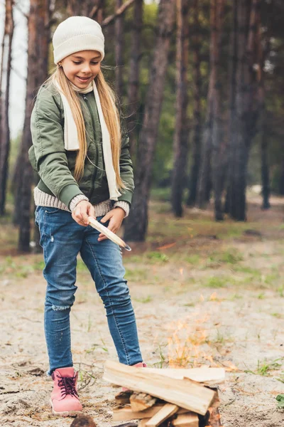 Chica añadiendo madera a la hoguera - foto de stock