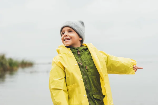 Junge im Regenmantel zeigt aufs Meer — Stockfoto
