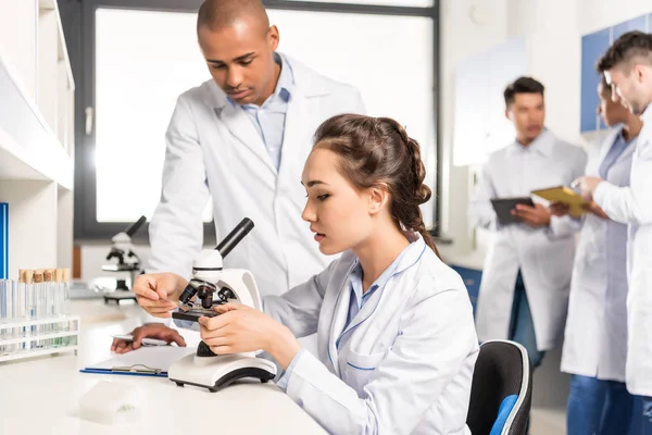 Químicos trabajando con microscopio - foto de stock