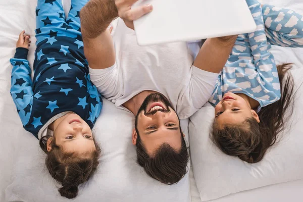 Father and daughters using tablet in bed — Stock Photo
