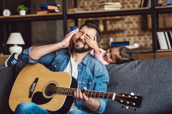 Hija cubriendo ojos de padre con guitarra - foto de stock