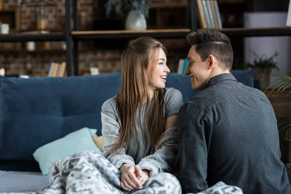 Glückliches Paar, das morgens auf dem Bett sitzt und einander ansieht — Stockfoto