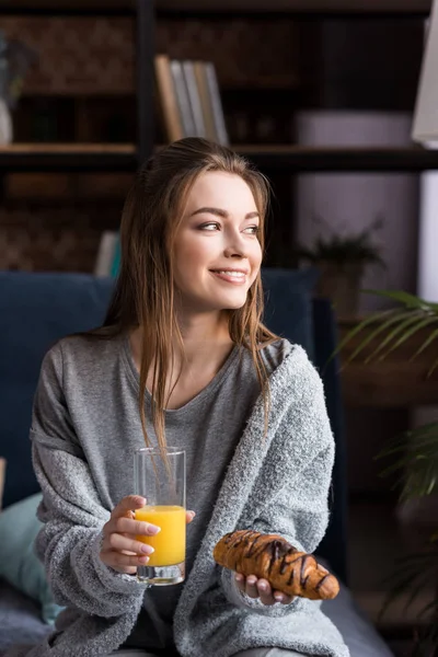 Sonriente chica sosteniendo vaso de jugo de naranja y croissant en la mañana - foto de stock