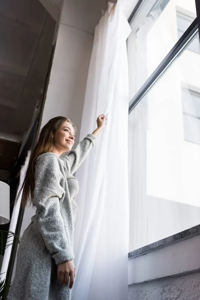 Вид снизу девушки, стоящей у окна и открывающей тюль — стоковое фото