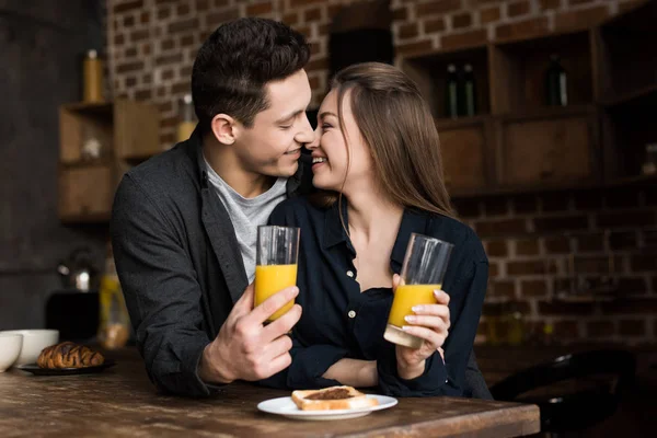 Casal sorrindo com suco de laranja vai beijar na cozinha — Fotografia de Stock