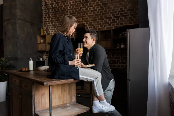 Coppia sorridente con succo d'arancia che si guarda in cucina — Foto stock