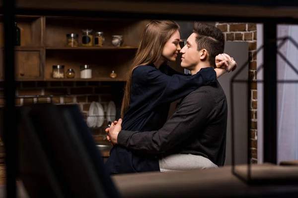 Girlfriend sitting on table in kitchen and going to kiss boyfriend — Stock Photo