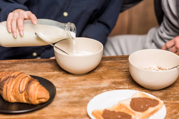 Immagine ritagliata di fidanzata versando il latte nel piatto — Foto stock