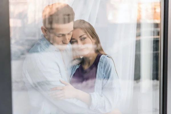 View through window on couple hugging and looking away — Stock Photo