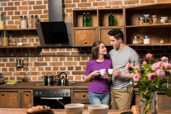 Paar schaut sich in Küche an und hält Kaffeetassen in der Hand — Stockfoto