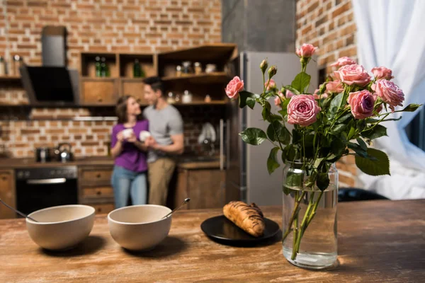 Casal com café na cozinha, pratos e buquê em primeiro plano — Fotografia de Stock