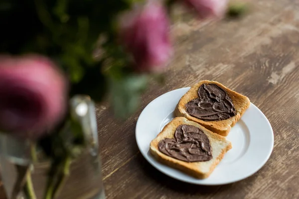 Toasts with chocolate paste in shape of hearts on wooden table, valentines day concept — Stock Photo