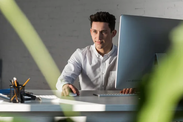 Sonriente empresario reflexivo sentado en el lugar de trabajo en la oficina moderna - foto de stock