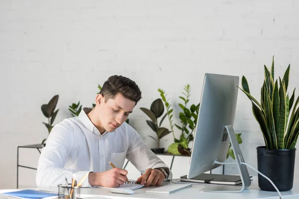 Concentrato giovane imprenditore prendere appunti sul posto di lavoro — Foto stock