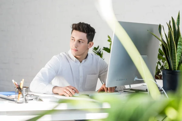 Nachdenklicher junger Geschäftsmann sitzt am Arbeitsplatz und schaut weg — Stockfoto