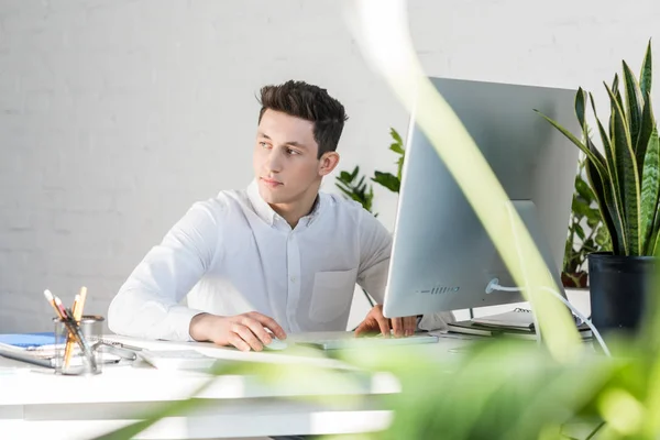 Jeune homme d'affaires réfléchi assis sur le lieu de travail et détournant les yeux — Photo de stock