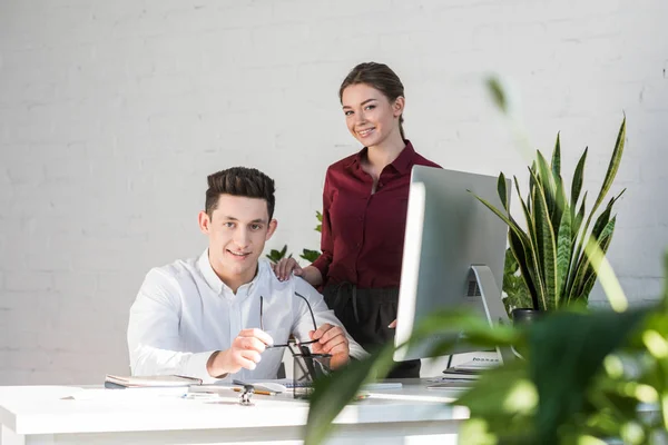 Sorrindo jovens gerentes olhando para a câmera no local de trabalho no escritório moderno — Fotografia de Stock