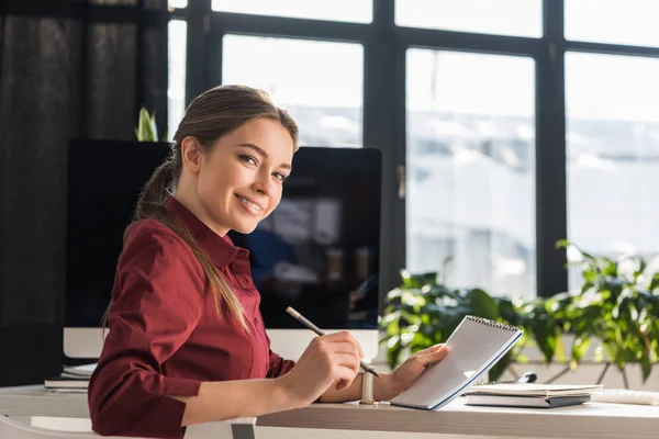 Felice giovane donna d'affari prendere appunti sul posto di lavoro — Foto stock