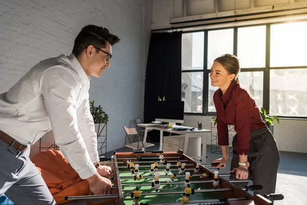 Jóvenes socios de negocios jugando futbolín en la oficina moderna - foto de stock