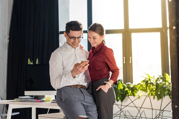 Feliz pareja de empresarios en la oficina moderna utilizando el teléfono inteligente juntos - foto de stock
