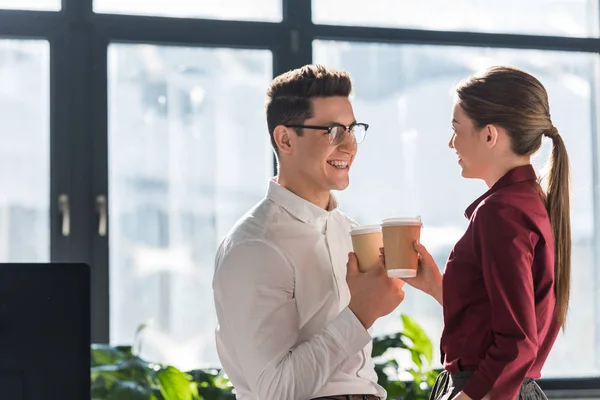 Happy colleagues with paper cups of coffee talking and flirting — Stock Photo