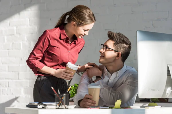 Happy young managers with coffee to go flirting at office — Stock Photo