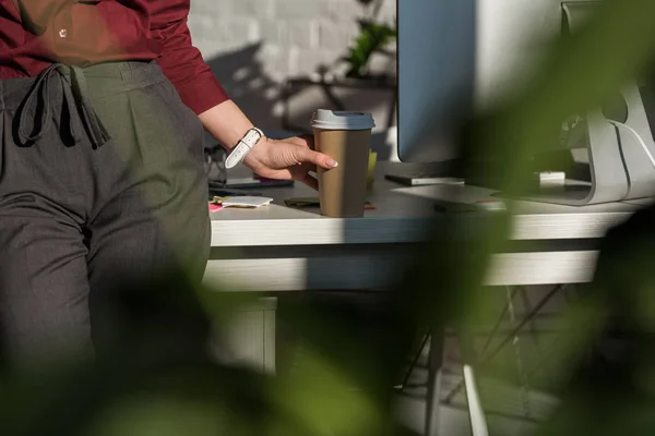 Cropped shot fo businesswoman with paper cup of coffee leaning back on work desk — Stock Photo