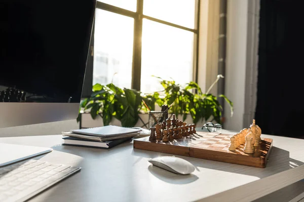 Close-up shot of chess board at modern workplace with computer — Stock Photo