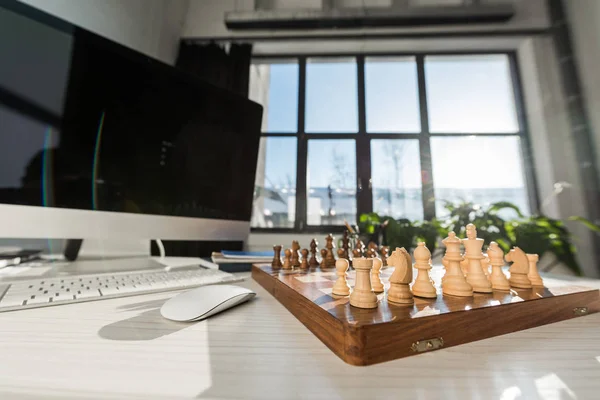 Close-up shot of chess board at workplace with computer — Stock Photo