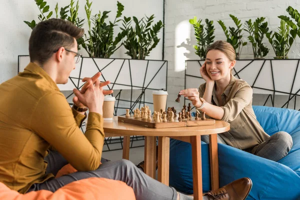 Молода щаслива пара грає в шахи, сидячи на мішках — стокове фото