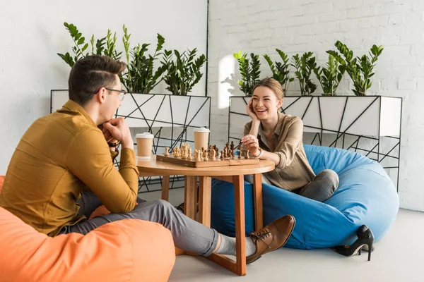 Young happy friends playing chess while sitting on beanbags — Stock Photo