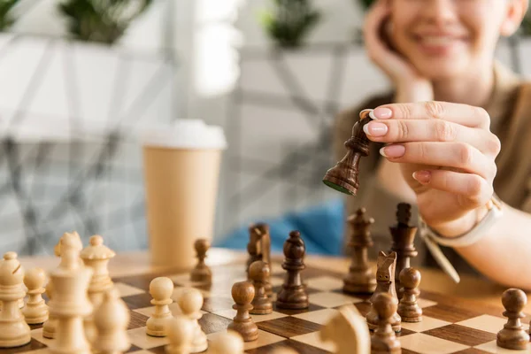 Обрезанный снимок молодой улыбающейся женщины, играющей в шахматы — стоковое фото
