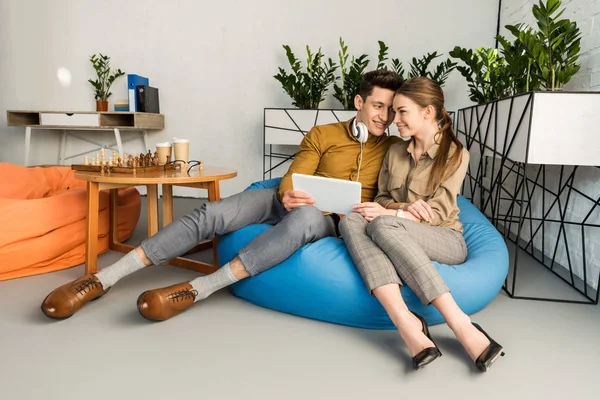 Молодая пара обнимается с помощью планшета вместе, сидя в бобовом мешке — стоковое фото
