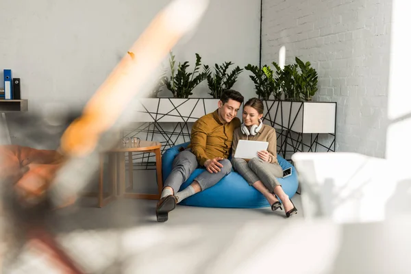 Счастливая молодая пара, используя планшет вместе, сидя в бобовом мешке — стоковое фото