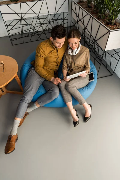 Vista de ángulo alto de pareja joven usando tableta juntos mientras están sentados en bolsa de frijoles - foto de stock