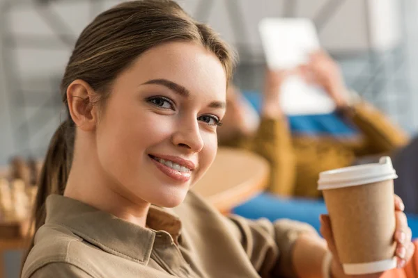 Крупним планом портрет усміхненої молодої жінки з паперовою чашкою кави — стокове фото