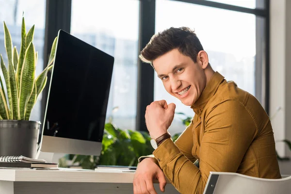 Feliz joven empresario celebrando el éxito en el lugar de trabajo y mirando a la cámara - foto de stock