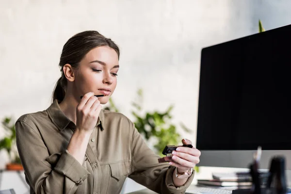 Hermosa joven haciendo maquillaje en el lugar de trabajo - foto de stock