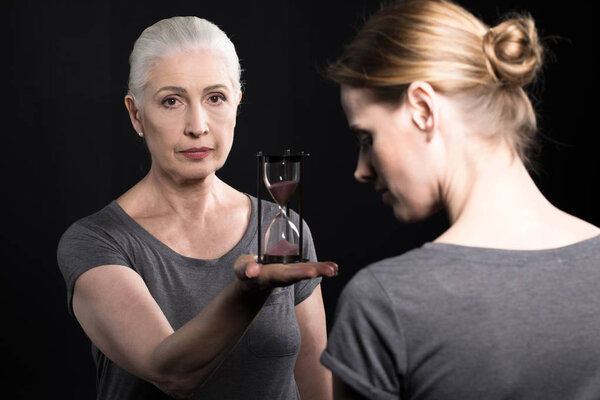 senior woman giving hourglass to daughter