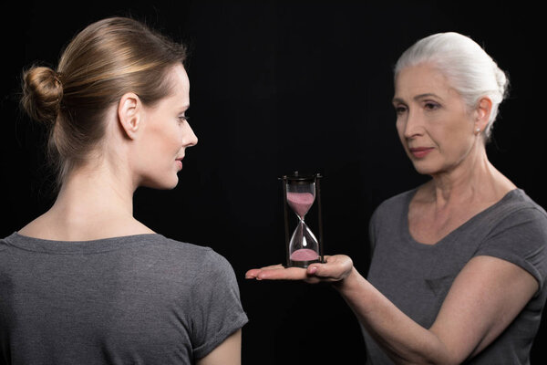 senior woman giving hourglass to daughter