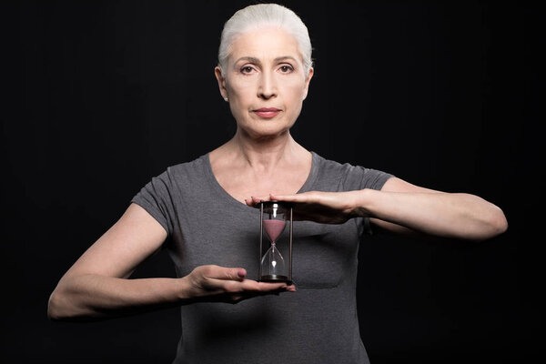 старшая женщина держит песочные часы
