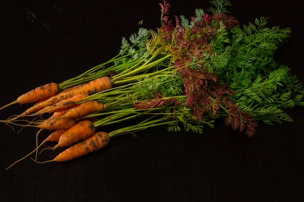 Fresh, farmer, young carrots with a beautiful tops on a black painted wooden background