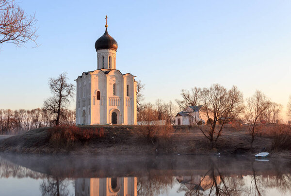 Туманное озеро с лодкой перед церковью ранней весной в dawn

