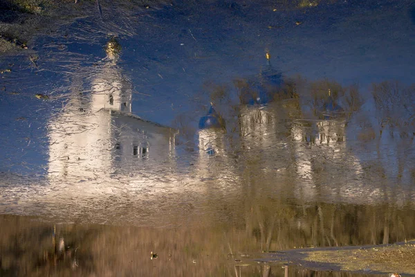 White-stone monastery with sky-blue domes, reflected in the edge of the last winter ice