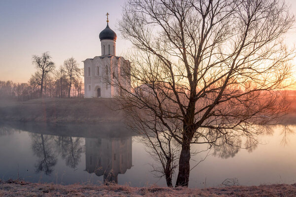 Туманное озеро с лодкой перед церковью ранней весной в dawn
