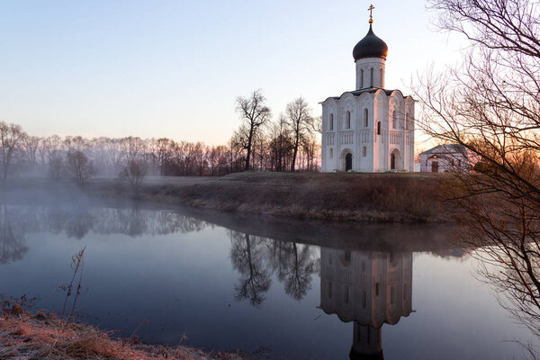Туманное озеро с лодкой перед церковью ранней весной в dawn
