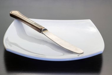 Bıçak çapraz olarak karanlık bir arka plan üzerinde beyaz bir plaka üzerinde yatıyor.