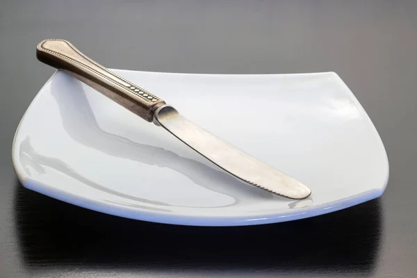 Cuchillo se encuentra en diagonal sobre un plato blanco sobre un fondo oscuro —  Fotos de Stock