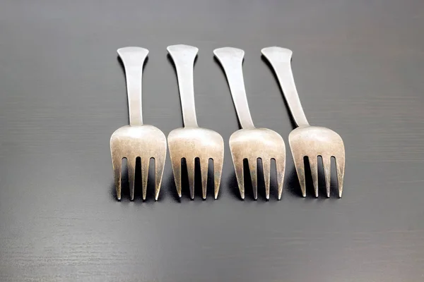 A row of four forks on a dark wooden background — Stock Photo, Image